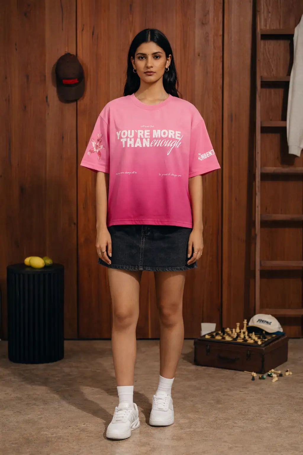Woman wearing a pink t-shirt with text in a room with wooden walls and shelves.