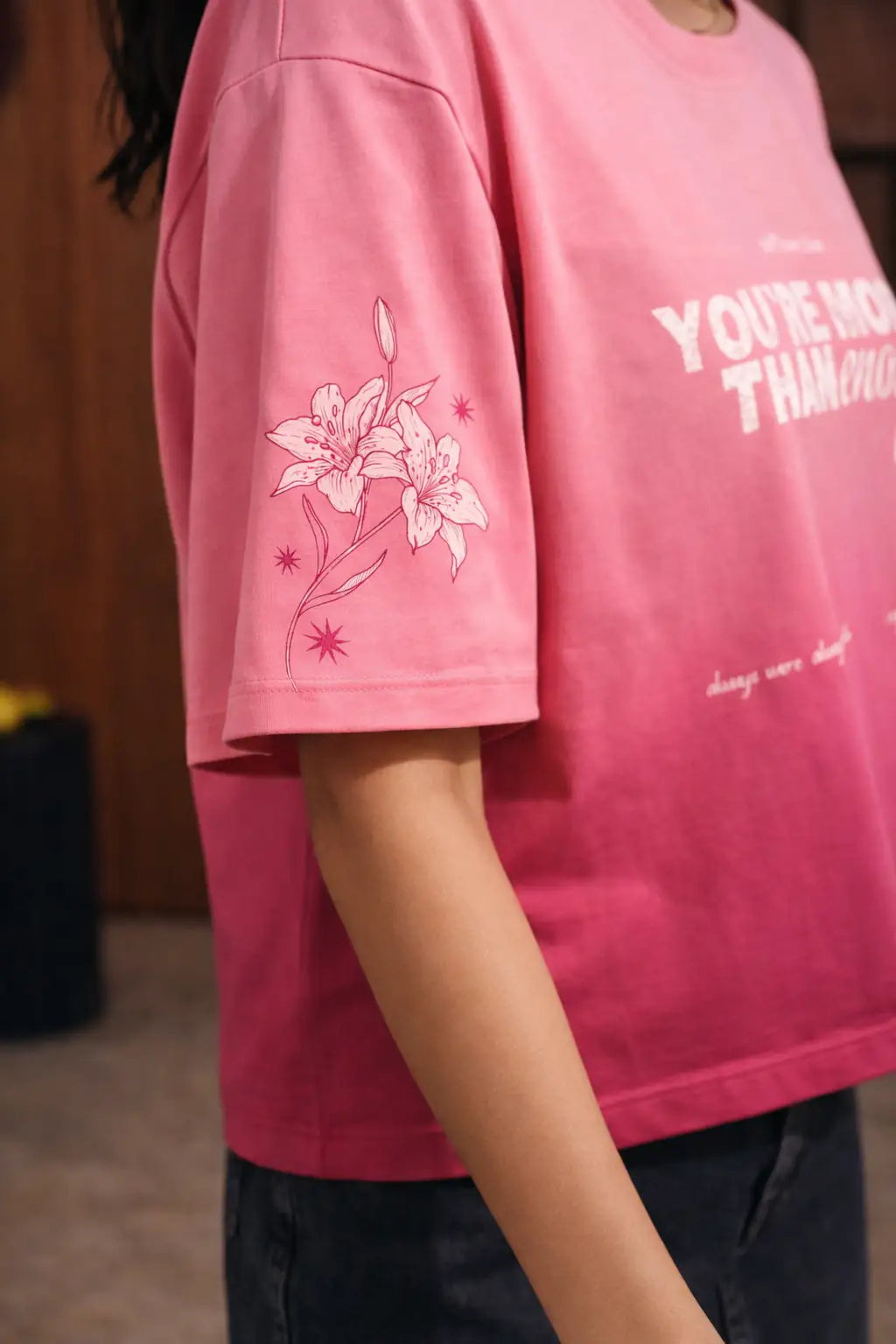 Person wearing a pink t-shirt with floral design and text.