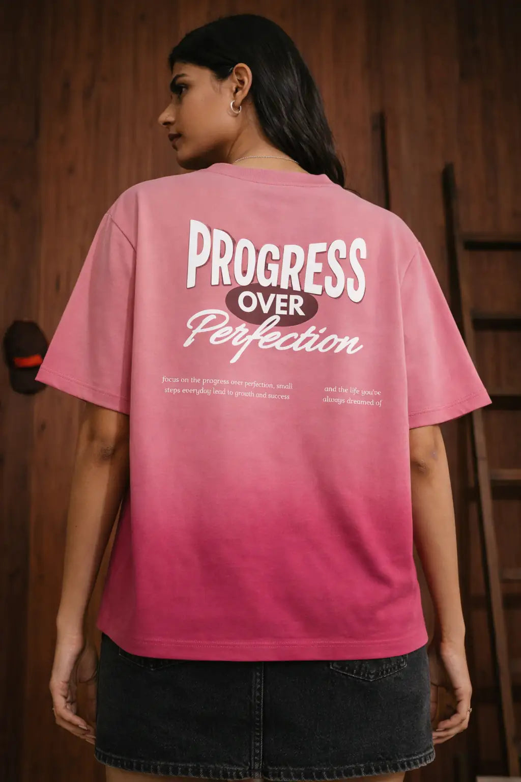 Person wearing a pink t-shirt with 'Progress Over Perfection' text on the back.