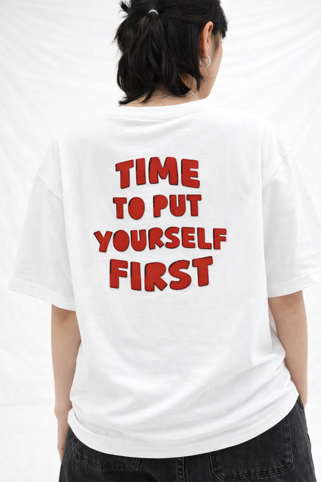 Person wearing a white t-shirt with red text on the back, 'TIME TO PUT YOURSELF FIRST'.